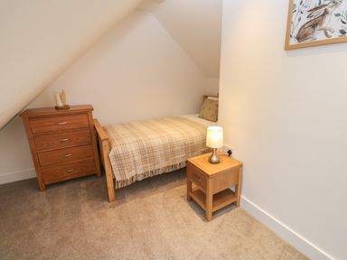 A bedroom with a single bed with plaid blanket a wooden bedside table with lamp and a wooden chest of drawers at Pol View Gunwalloe near Helston