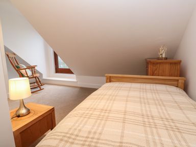 A bedroom with a single bed a wooden rocking chair a bedside table with a lamp and a wooden cabinet at Pol View Gunwalloe near Helston