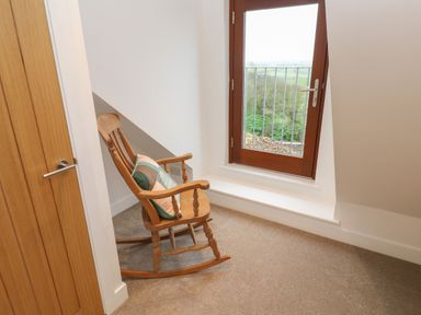 A rocking chair with a cushion next to a glass door with a metal railing and a view outside at Pol View in Gunwalloe near Helston