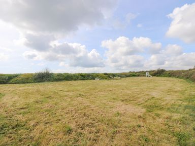 A grassy field with bushes along the edge and a small playground slide at Pol View in Gunwalloe near Helston