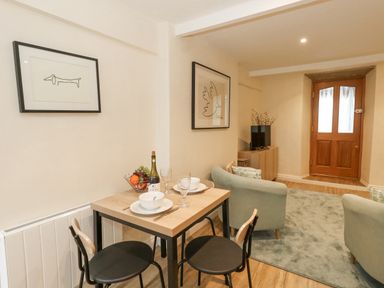 A small dining table with two chairs a living area with two armchairs a TV on a cabinet and a wooden door at Bobbin Cottage in Swanage