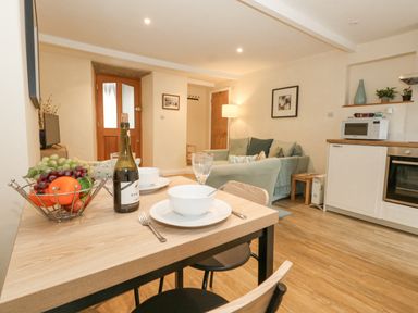 A kitchen and living area with a wooden table set for two with bowls a bottle of wine and a fruit basket at Bobbin Cottage in Swanage