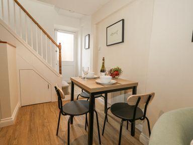 A small dining area with a table set for two and a staircase in the background at Bobbin Cottage in Swanage