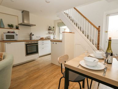A kitchen area with white cabinets a wooden countertop an oven and microwave stairs and a dining table set with bowls glasses and cutlery