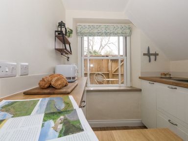 A kitchen with a window above the countertop and bread on a cutting board at Bobbin Cottage in Swanage