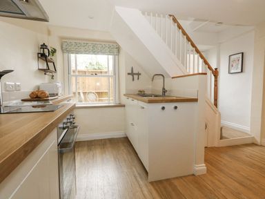 A kitchen with wooden countertops a window a sink and a staircase in Bobbin Cottage in Swanage