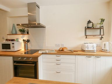 A kitchen countertop with a microwave oven a cutting board with bread a four-slot toaster a kettle and kitchen utensils at Bobbin Cottage in Swanage