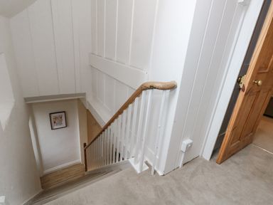 A staircase with a wooden handrail and white spindles next to a wooden door at Bobbin Cottage in Swanage