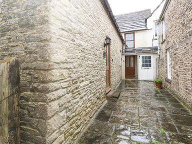 A stone paved courtyard between stone buildings with wooden and white doors at Bobbin Cottage in Swanage