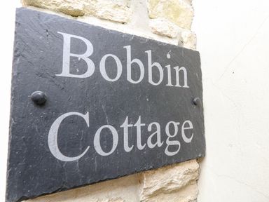 A slate sign with the words Bobbin Cottage mounted on a stone wall at Bobbin Cottage in Swanage