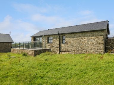 A stone cottage with a glass railing balcony and green grass in front at Tyddyn Bach in Rhydwyn