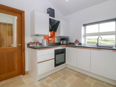 A kitchen with white cabinets black countertop an oven a kettle a knife block and a window at Tyddyn Bach in Rhydwyn