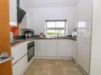 A kitchen with white cabinets a black countertop a window a built in oven and a wooden door at Tyddyn Bach in Rhydwyn