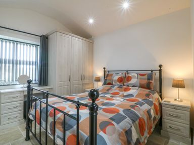 A bedroom with a patterned bedspread a black metal bed frame a wardrobe side tables and a window with blinds at Tyddyn Bach in Rhydwyn