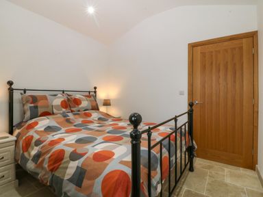 A bedroom with a patterned bedspread on a metal bed frame a wooden door a bedside table and a lamp at Tyddyn Bach in Rhydwyn