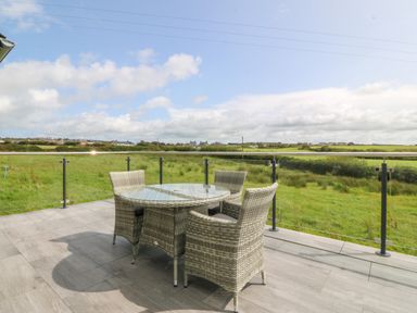 A balcony with a round glass table and four wicker chairs overlooking green fields at Tyddyn Bach in Rhydwyn