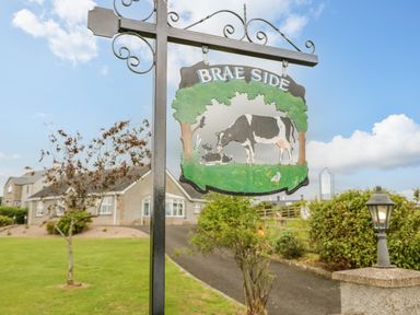 A metal sign with pictures of cows and the text brae side near a driveway and a house at Braeside Farm House in Cloughmills