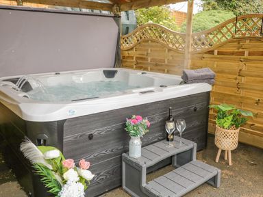 An outdoor hot tub with water jets under a wooden canopy with towels flowers a bottle of wine and glasses at Braeside Farm House in Cloughmills