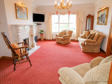 A living room with armchairs a sofa a wooden rocking chair a fireplace and a wall-mounted television at Braeside Farm House in Cloughmills