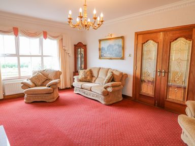 A living room with beige sofas a red carpet wooden double doors a chandelier and a glass display cabinet at Braeside Farm House in Cloughmills