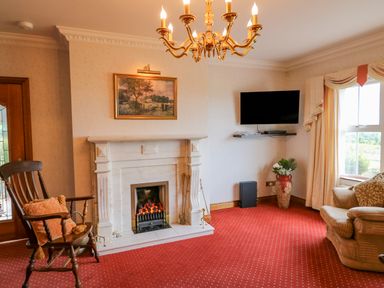 A living room with a wooden chair with cushion a fireplace a mounted TV and a sofa at Braeside Farm House in Cloughmills