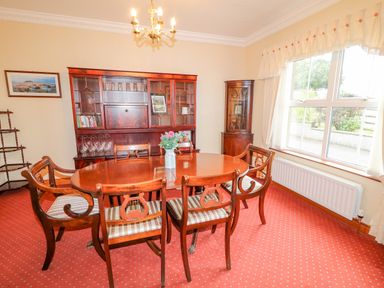 A dining room with wooden table and chairs a cabinet with glassware and a large window at Braeside Farm House in Cloughmills