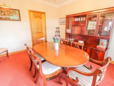 A dining room with wooden table and chairs a cabinet with glassware and flowers on table at Braeside Farm House in Cloughmills