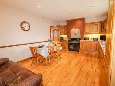 A kitchen with wooden cabinets a dining table with chairs and a brown leather sofa at Braeside Farm House in Cloughmills