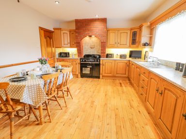 A kitchen with wooden cabinets a dining table set with dishes and a stove with a brick chimney at Braeside Farm House in Cloughmills