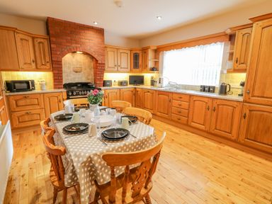 A kitchen with a dining table set for six in the center and wooden cabinets along the walls at Braeside Farm House in Cloughmills