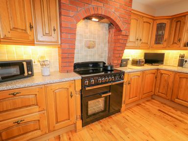 A kitchen with wooden cabinets black stove microwave and utensils at Braeside Farm House in Cloughmills
