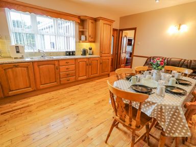 A kitchen with wooden cabinets a dining table set with plates cups and flowers and a brown leather sofa at Braeside Farm House in Cloughmills