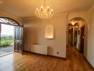 An entryway with wooden floor a chandelier a wooden door open to a garden and an arched doorway at Braeside Farm House in Cloughmills