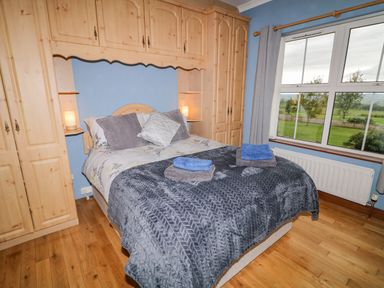 A bedroom with a bed with pillows and folded towels next to a window and wooden wardrobes at Braeside Farm House in Cloughmills