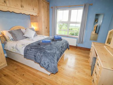 A bedroom with a bed towels on it wooden wardrobes and a window at Braeside Farm House in Cloughmills
