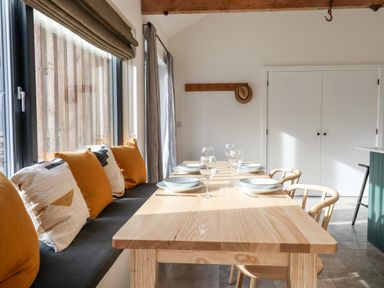 A dining area with a wooden table set with bowls and glasses a bench with cushions and wooden chairs at 1 Caddaford Barns in Buckfastleigh