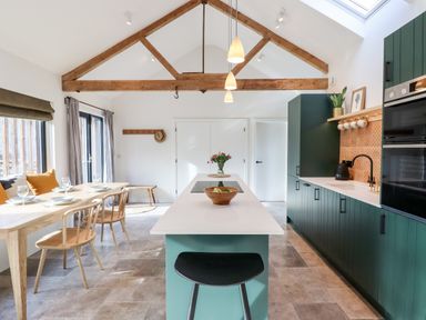 A kitchen with green cabinets a dining table with chairs and wooden beams on the ceiling at 1 Caddaford Barns in Buckfastleigh