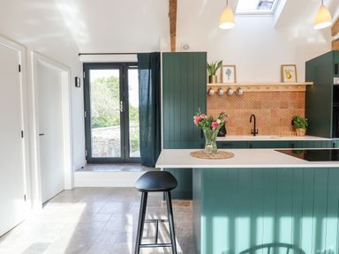 A kitchen with green cabinetry a white countertop a black stool and glass doors at 1 Caddaford Barns in Buckfastleigh