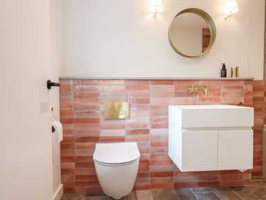 A bathroom with a wall-mounted toilet and a white floating vanity unit with a round mirror and two wall lamps at 1 Caddaford Barns in Buckfastleigh