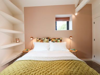 A bedroom with a double bed two side tables lamps and corner shelves at 1 Caddaford Barns in Buckfastleigh