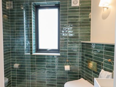 A bathroom with green tiled walls a window a toilet a toilet paper holder and a towel ring at 1 Caddaford Barns Buckfastleigh
