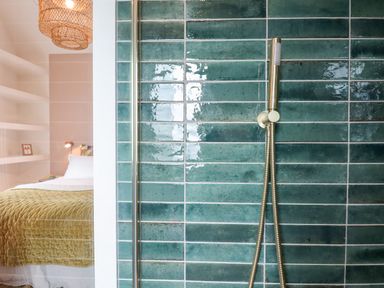 A bathroom with green tiles and a handheld shower head next to a bedroom with a bed and pendant light at 1 Caddaford Barns in Buckfastleigh