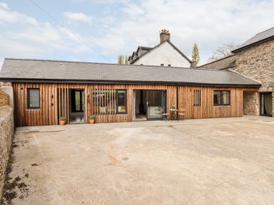 A wooden barn style house with stone walls and a concrete courtyard at 1 Caddaford Barns in Buckfastleigh