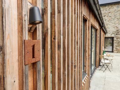 A wooden exterior wall with a number 1 sign and a black outdoor light at 1 Caddaford Barns Buckfastleigh