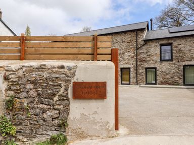 Exterior of a stone building with a sign reading caddaford barns and a wooden fence at 1 Caddaford Barns in Buckfastleigh