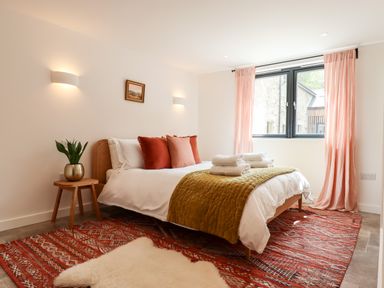 A bedroom with a bed near a window with pink curtains and a small wooden side table at 1 Caddaford Barns Buckfastleigh
