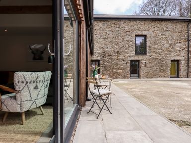 An outdoor patio area with a small table and two chairs near a stone building at 1 Caddaford Barns in Buckfastleigh