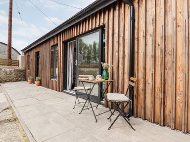 A patio with a small table and two chairs outside a wooden building at 1 Caddaford Barns in Buckfastleigh
