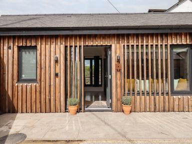 A wooden exterior wall with two windows and a door in the middle with potted plants on the patio at 1 Caddaford Barns Buckfastleigh