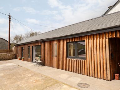 An exterior view of a wooden barn with windows a small table and two chairs outside at 1 Caddaford Barns in Buckfastleigh
